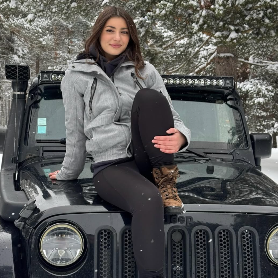 Woman sitting on a black Jeep in a snowy landscape