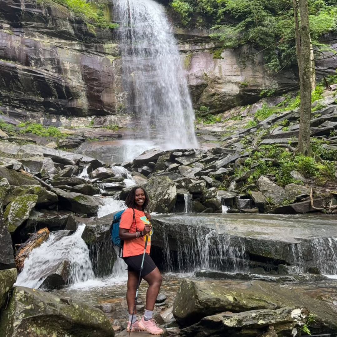 A woman hiker posed in front of a tall waterfall in the Great Smoky Mountains