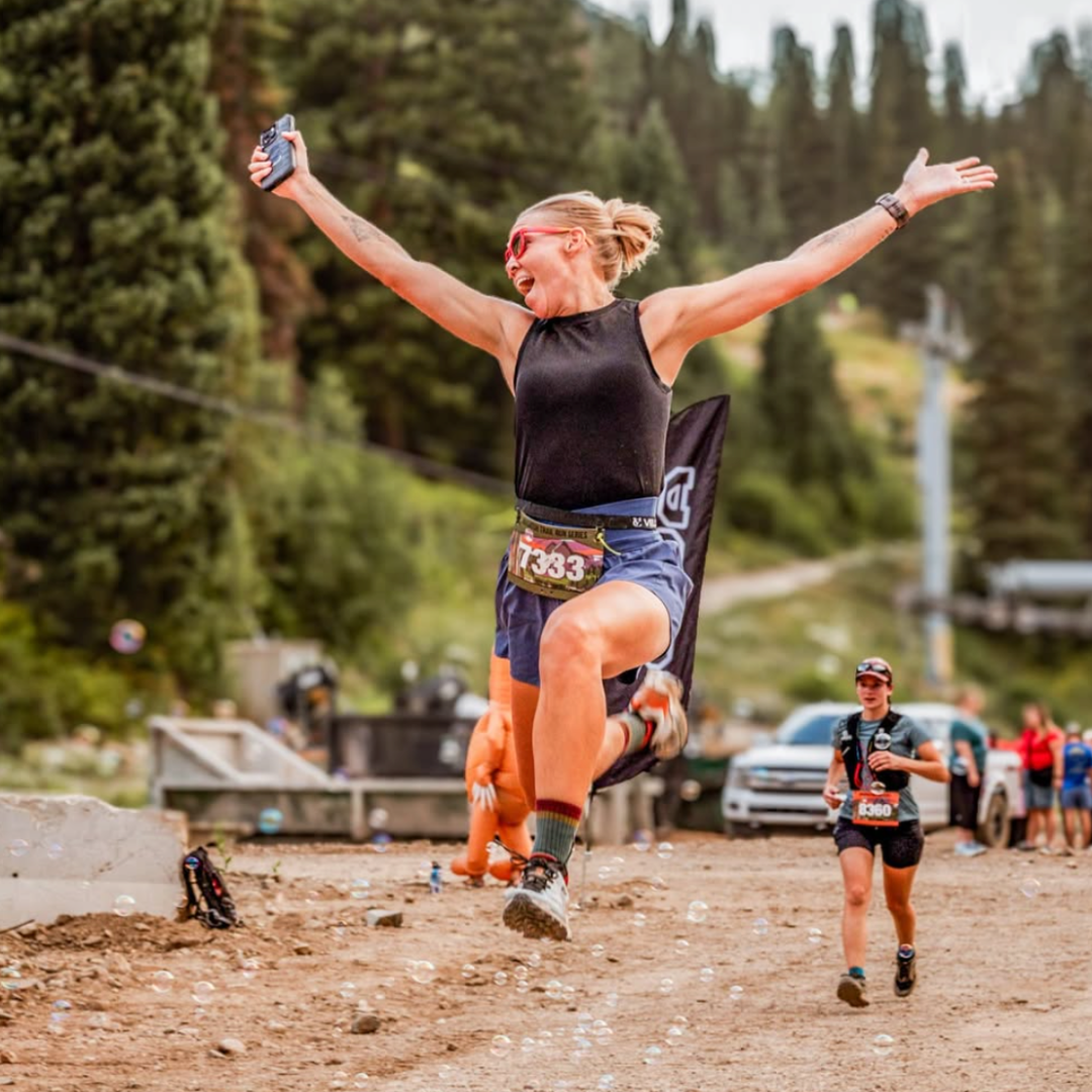 A woman leaping into the air on a mountain trail 