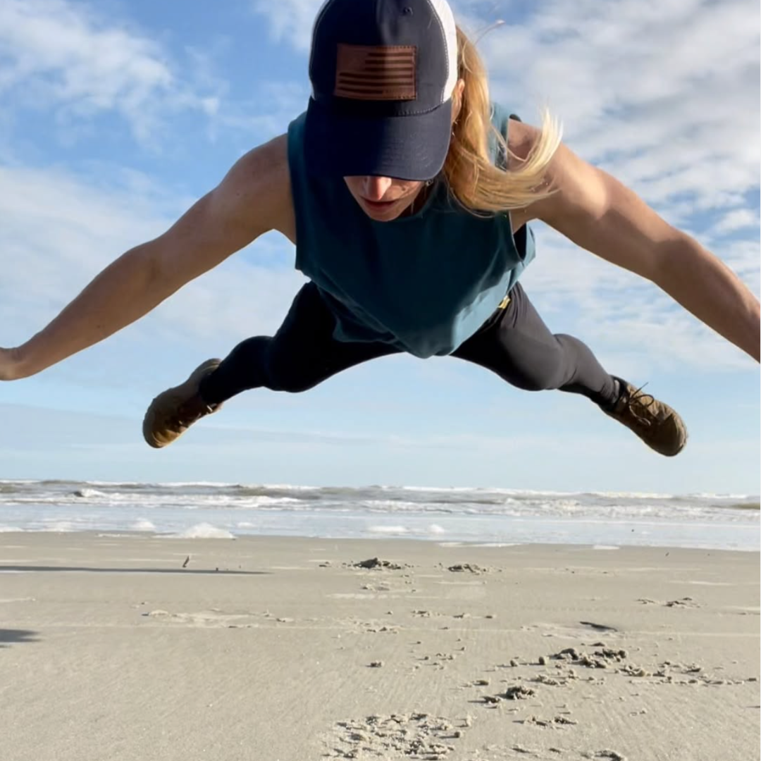 A woman with a ball cap and LOWA boots photographed hovering above the beach