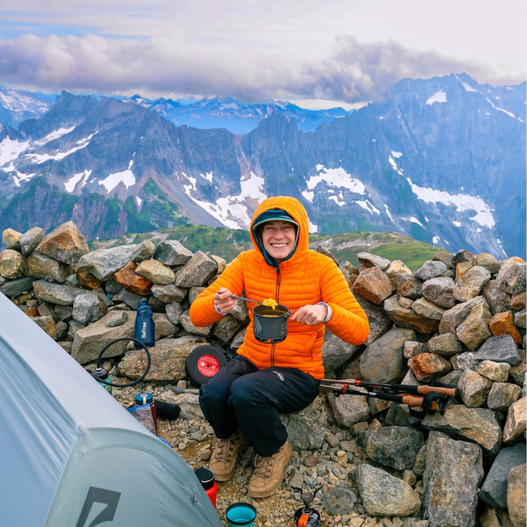 A woman sits on a mountaintop campsite with a meal. Posted by Instagram user @gwynandami. 