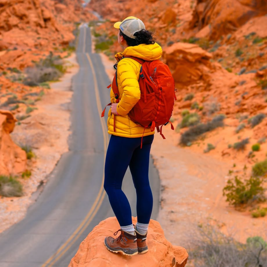 A person with a yellow jacket and red backpack standing on a desert overlook
