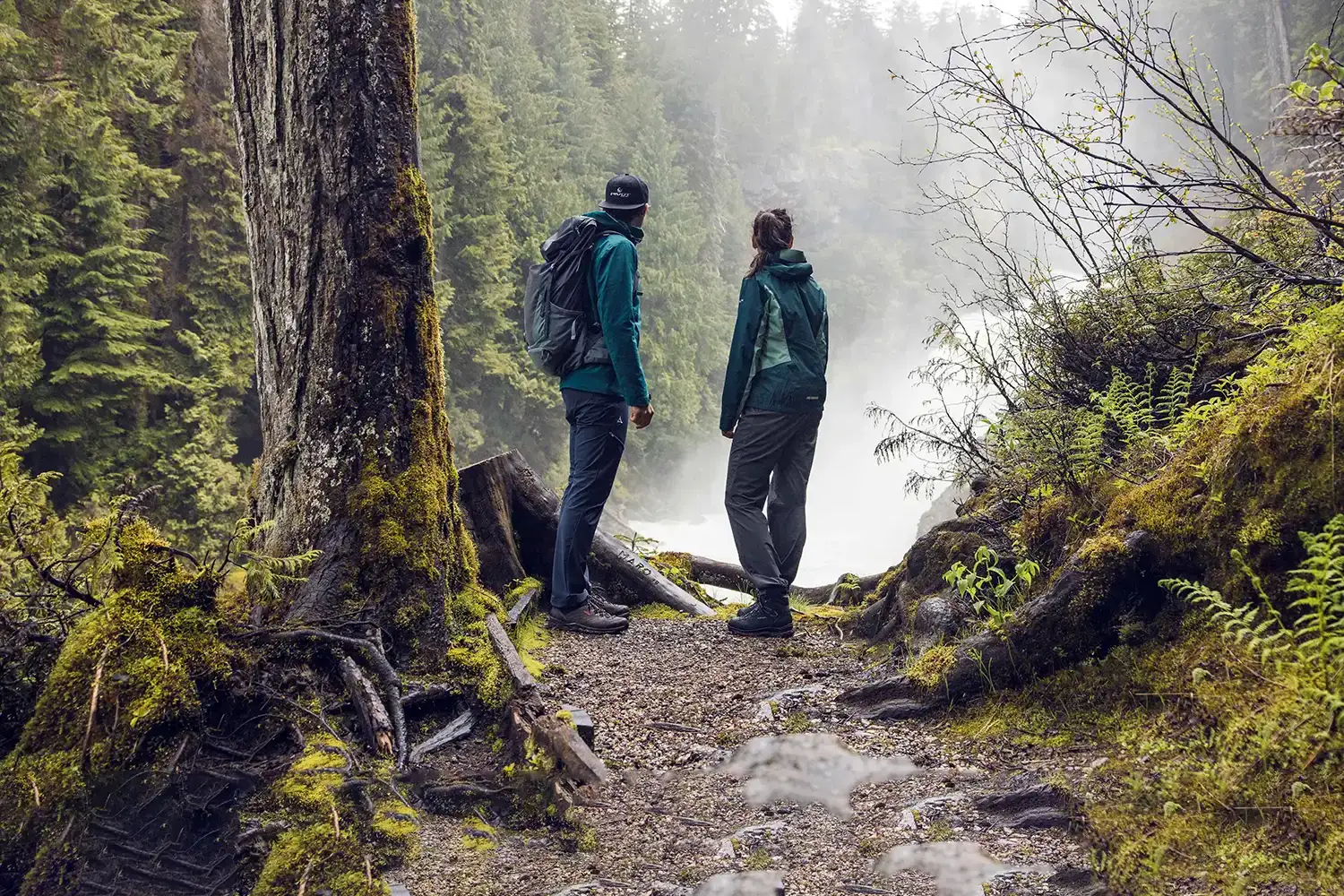 A couple backpackers in rainy forest looking out at river