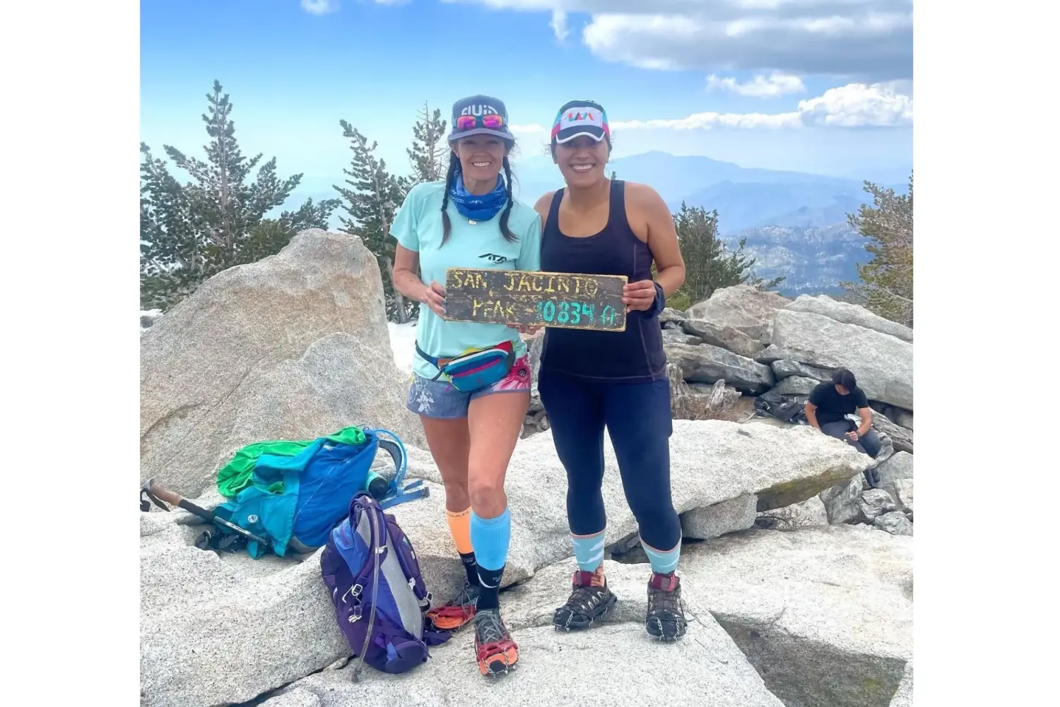 two women, one being cyndi wyatt, holding a sign of the summit of a peak, the sign reads :"San Jacinto peak 10,834 feet"
