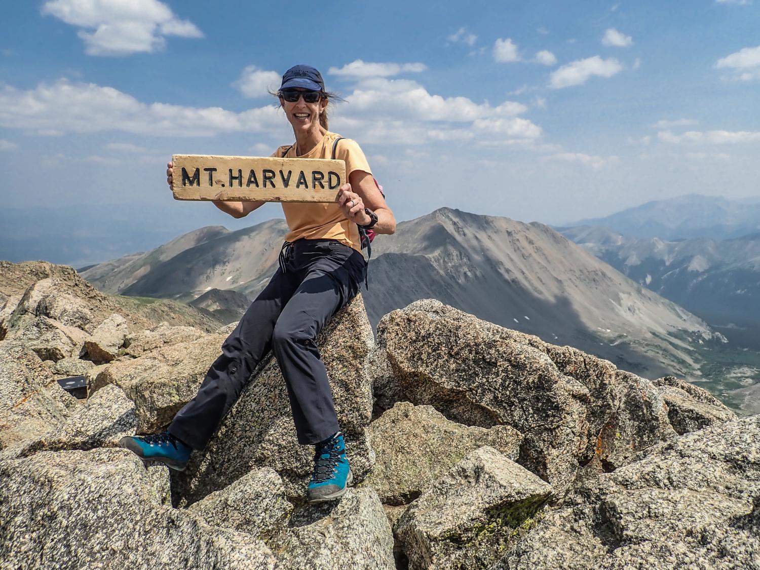 LOWA Ambassador Lisa Ballard holding a sign with "Mt. Harvard" written on it, standing at the summit of Mt. Harvard